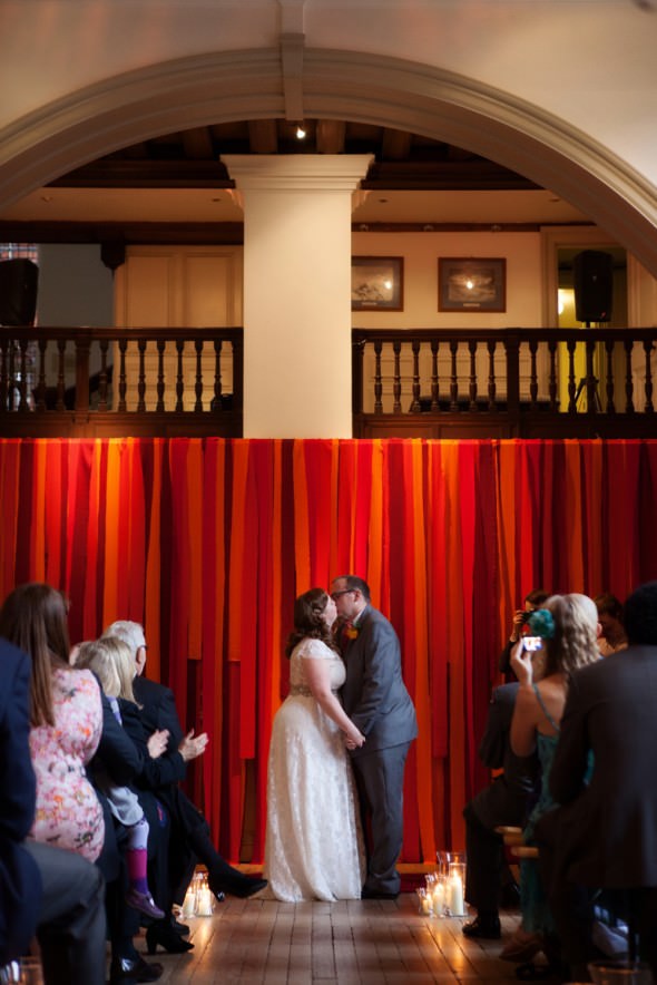 bride and groom first kiss at alter with ribbon backdrop