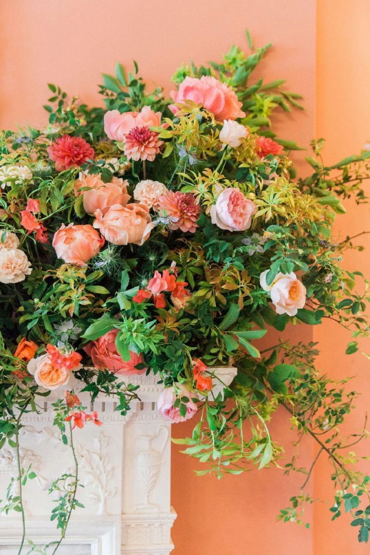 coral and peach wedding flowers on fireplacewith cascading foliage