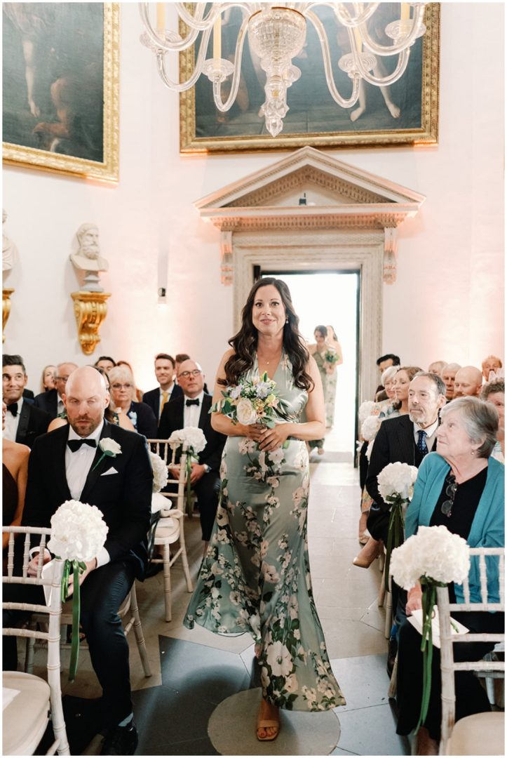 bridesmaid in sage green floral dress walking up aisle at Chiswick House Wedding