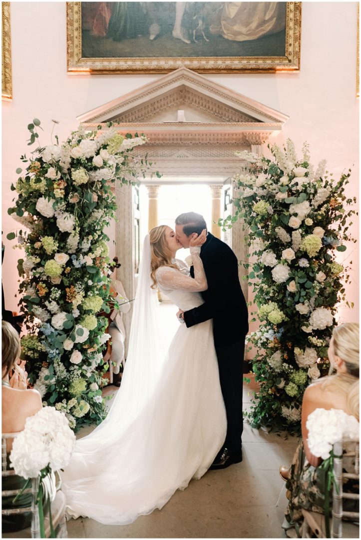 bride and groom first kiss flanked by tall floral arch at Chiswick House Wedding