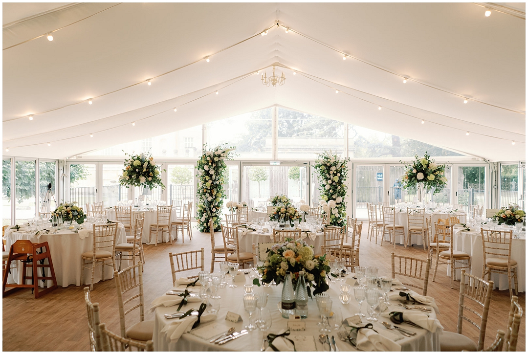 wedding reception with round tables with tall and low white floral arrangements with pops of peach and blue at Chiswick House Wedding
