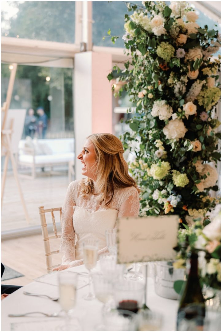 bride in lace dress watches speeches at Chiswick House Wedding